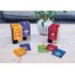 Auf dem Bild sind drei Happiness Is Teepackungen in den Farben lila, rot und gelb zu sehen. Diese stehen auf einem Tisch. Dahinter ist eine Pflanze zu sehen.